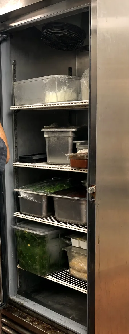 A refrigerated cabinet open on its shelves, the stainless door frame catching the light down one edge.