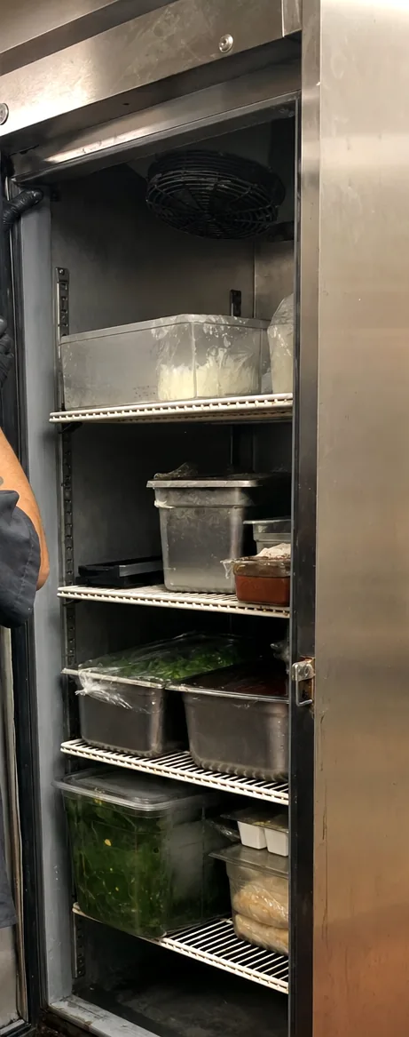 An upright refrigerated cabinet standing open, its racked shelving in shadow and the gasket line lit down the frame.