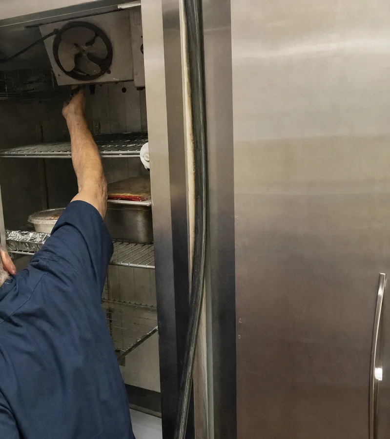 The fan bracket and upper shelf of an open refrigerated cabinet, an arm crossing the frame to reach it.