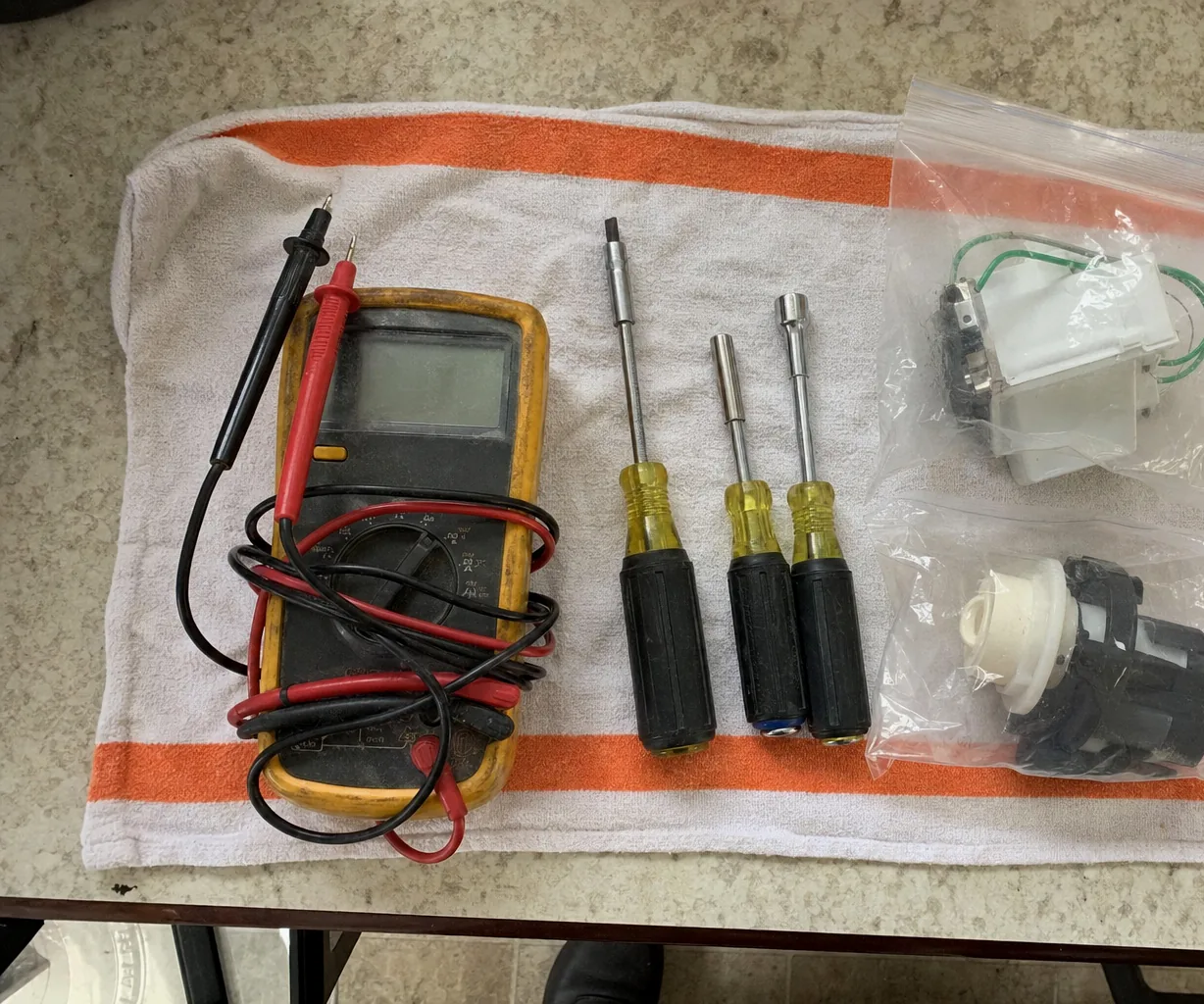 A digital multimeter and a row of nut drivers arranged on a towel on a kitchen floor.