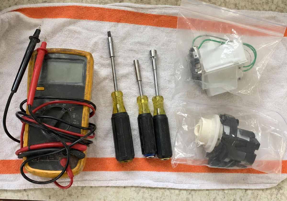 A worn multimeter beside nut drivers on a kitchen towel, the leads coiled loosely across it.