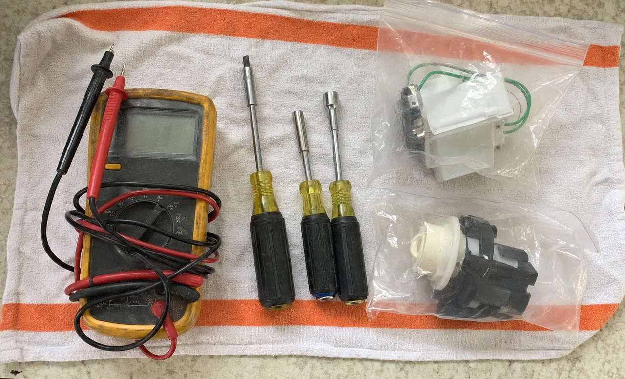 An overhead frame of hand tools and spare components on a towel laid on a hard kitchen floor.